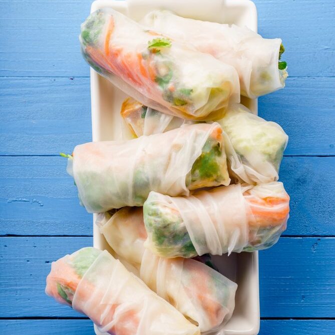 Rice paper rolls made with tofu, in a rectangular china dish sitting on a blue wooden table