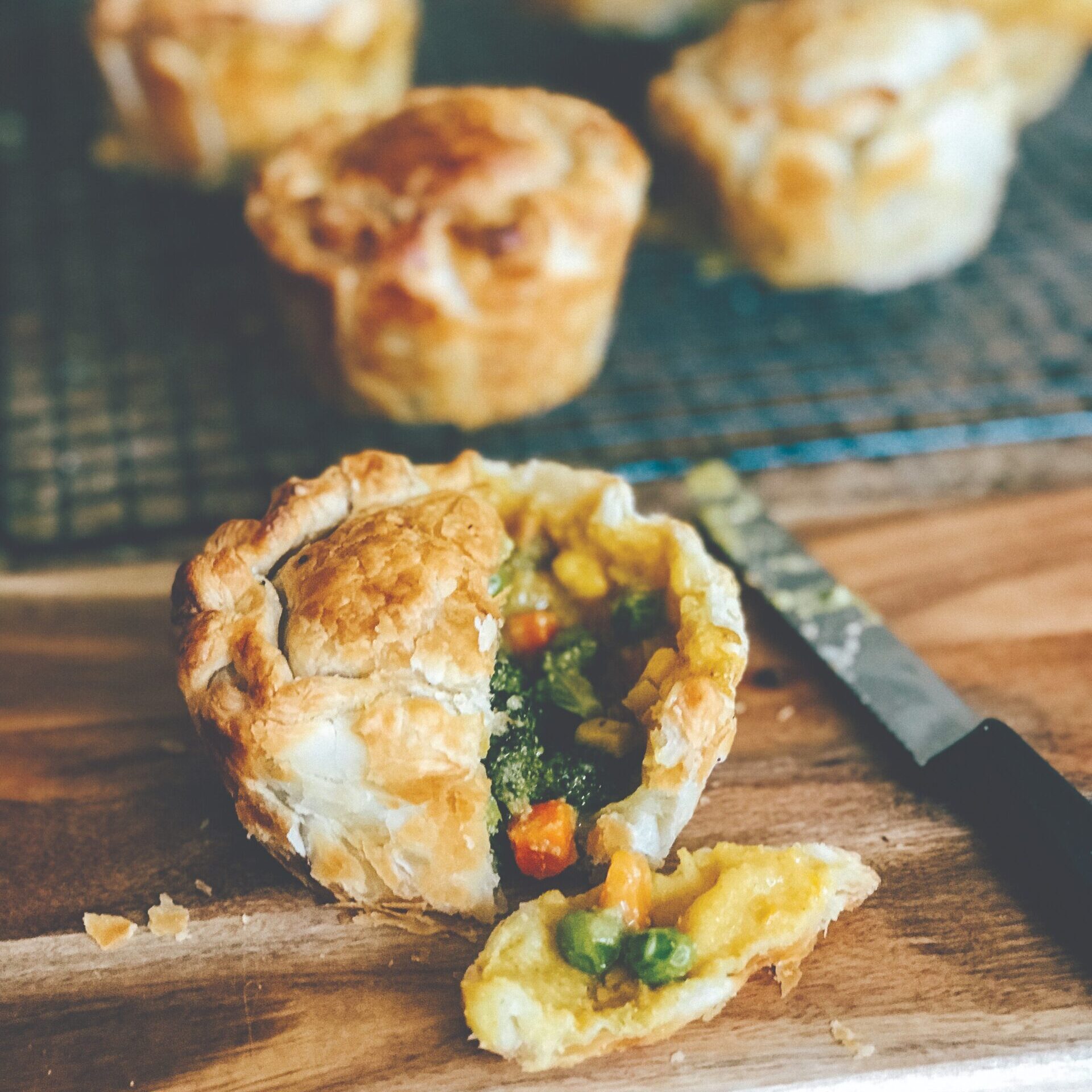 Pie on chopping board, cut open to reveal delicious veggie filling. Other pies visible on cooling rack in background.