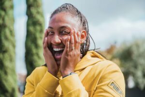 Sabrina in yellow top - hands on cheeks, with big smile