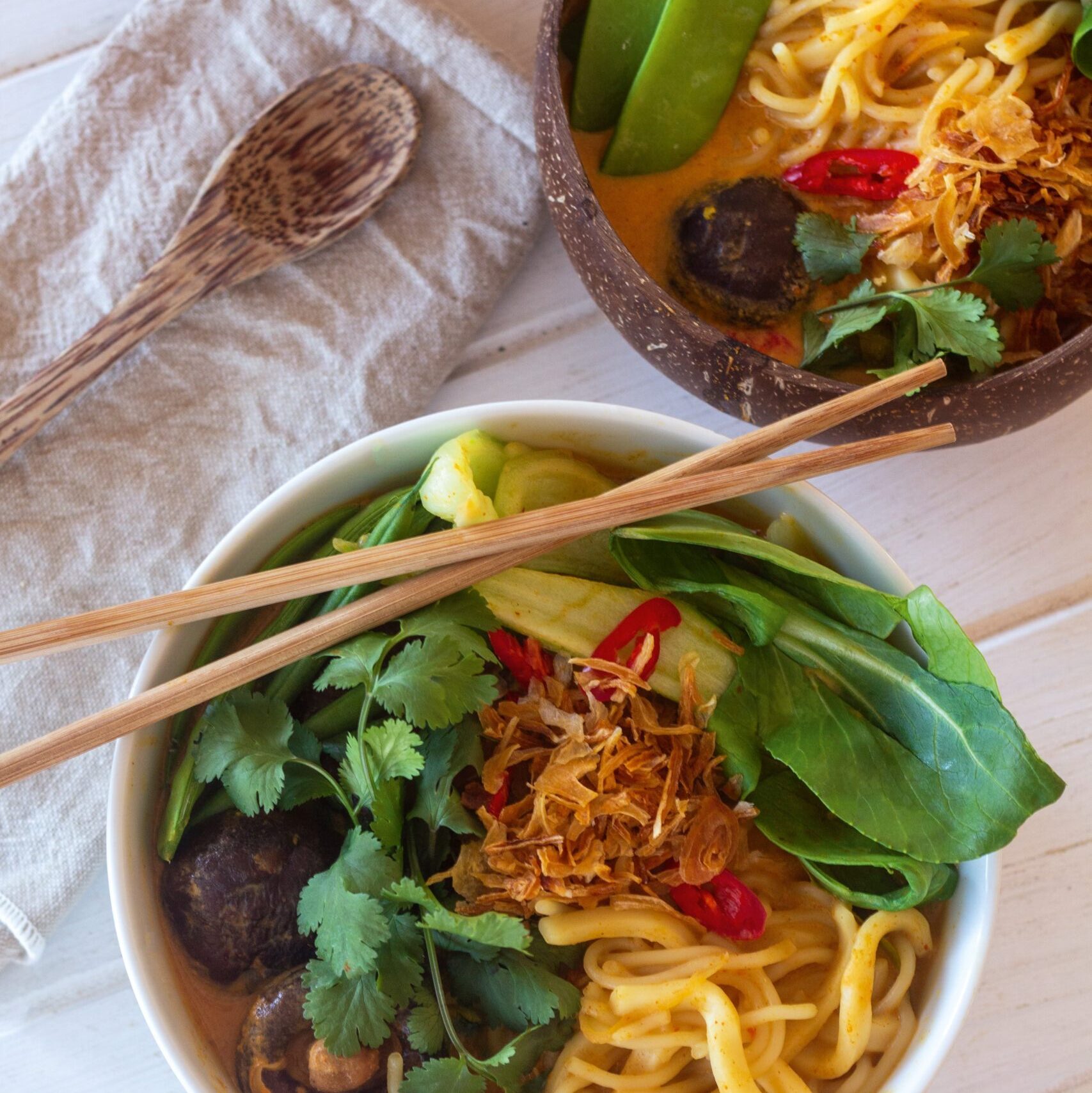 Two bowls of vegan ramen on white table with chopsticks and cloth napkin