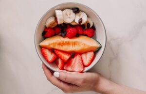 Hand holding fruit bowl with honeydew melon, banana and berries