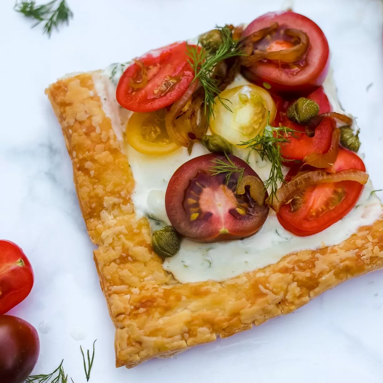 Whipped feta and tomato tart by YAY! Foods - slice on marble bench with cherry tomatoes and herbs